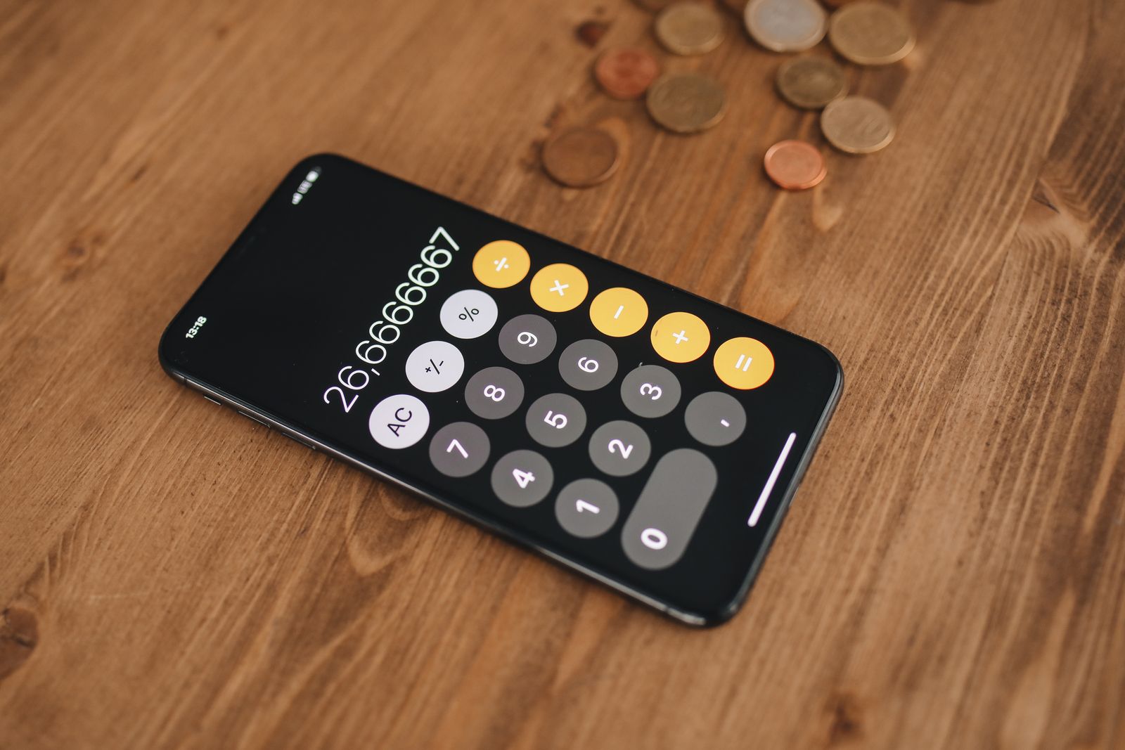 Smartphone affichant une calculatrice, avec des pièces de monnaie sur une table en bois
