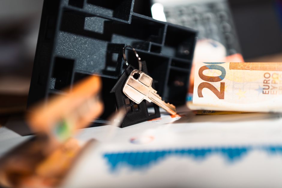 Clé de maison sur un porte-clés, billets de 20 euros et graphique sur une table