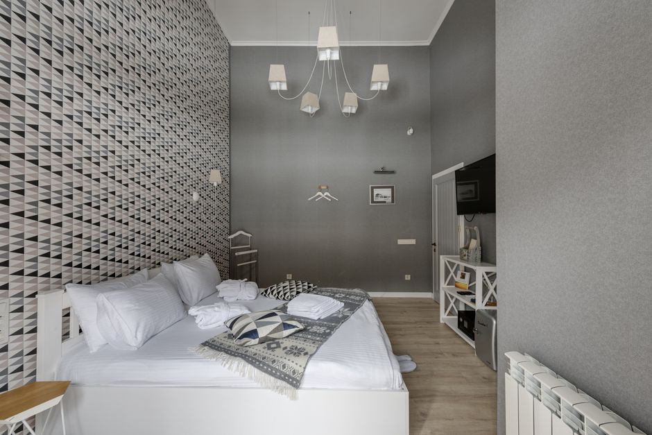 Chambre d’hôtel lumineuse avec lit blanc, plaid et mur à motifs géométriques