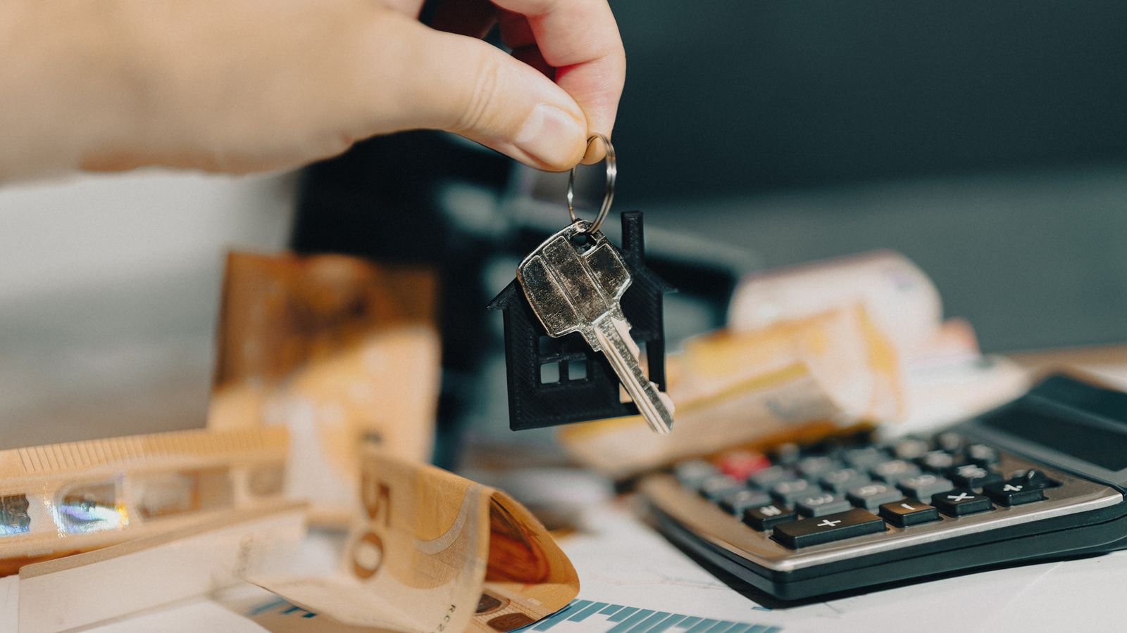 Clés d'un logement tenues au-dessus de billets en euros et d'une calculatrice