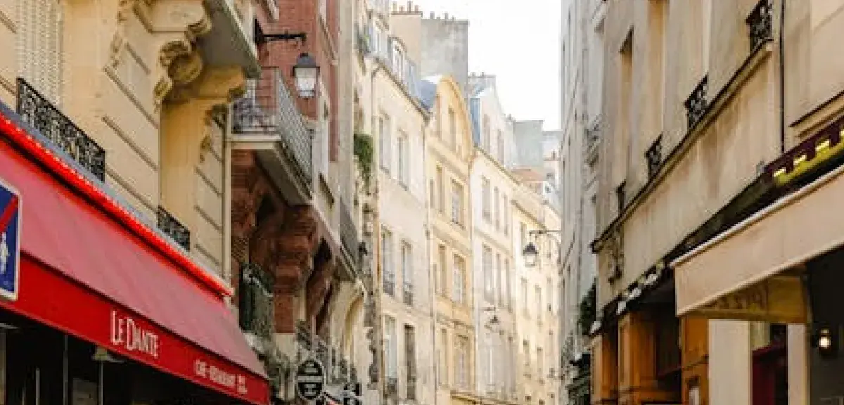 Rue parisienne typique bordée d'immeubles historiques et de commerces, illustrant le cadre urbain de la capitale