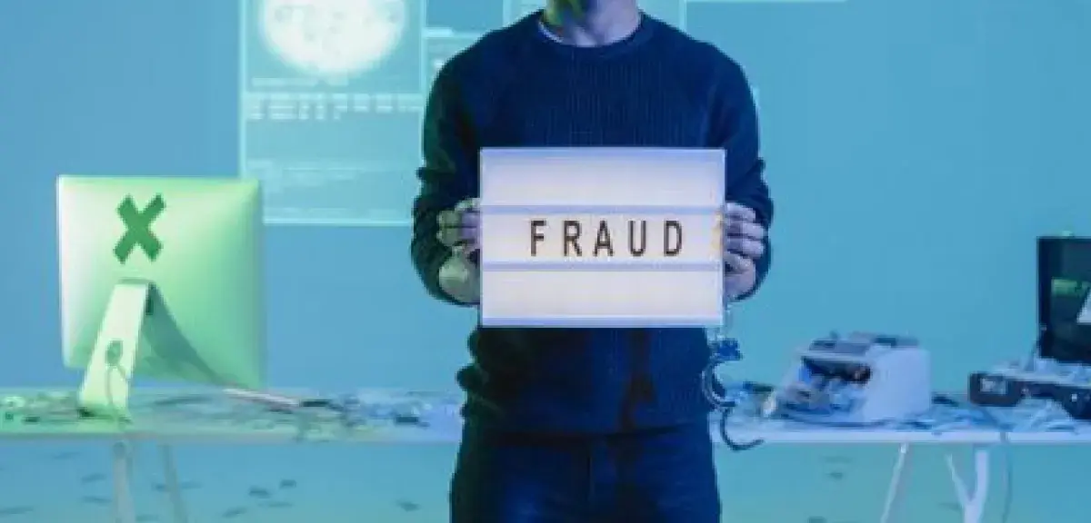 Young man holding a 'fraud' sign in a tech-focused setting with digital and cash elements.