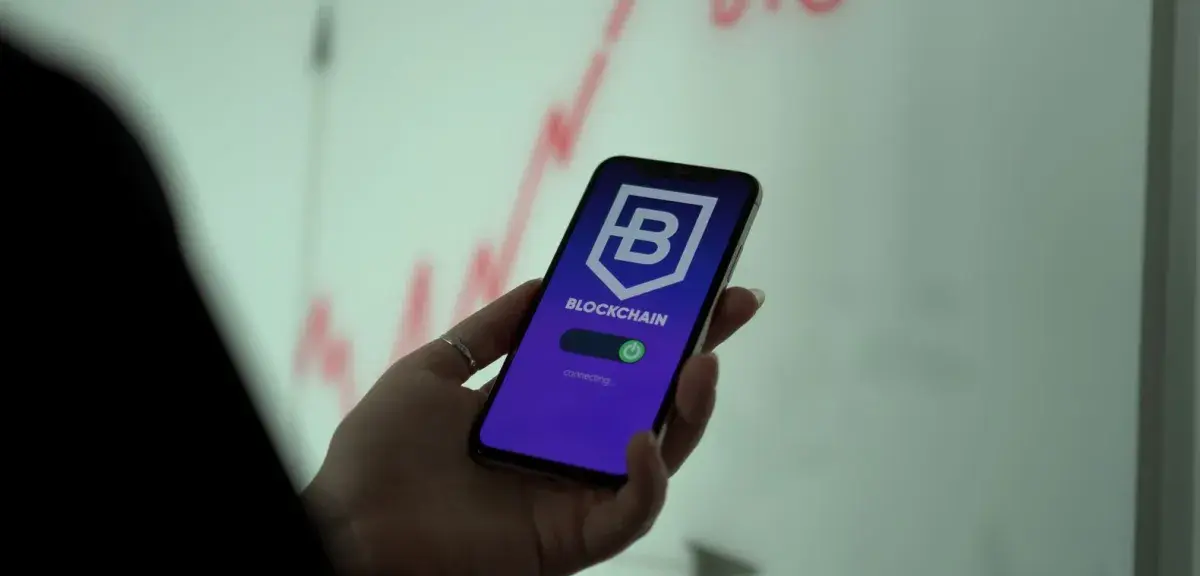 Une main tient un smartphone qui affiche une application de crypto-actifs