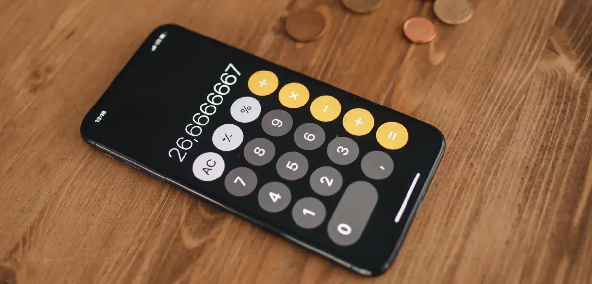 Smartphone affichant une calculatrice, avec des pièces de monnaie sur une table en bois