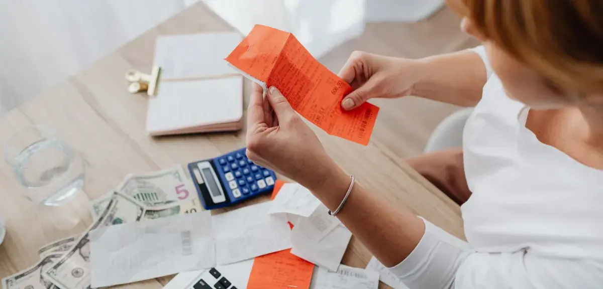 Une femme examine des tickets de caisse à côté d'une calculatrice et de billets, à son bureau