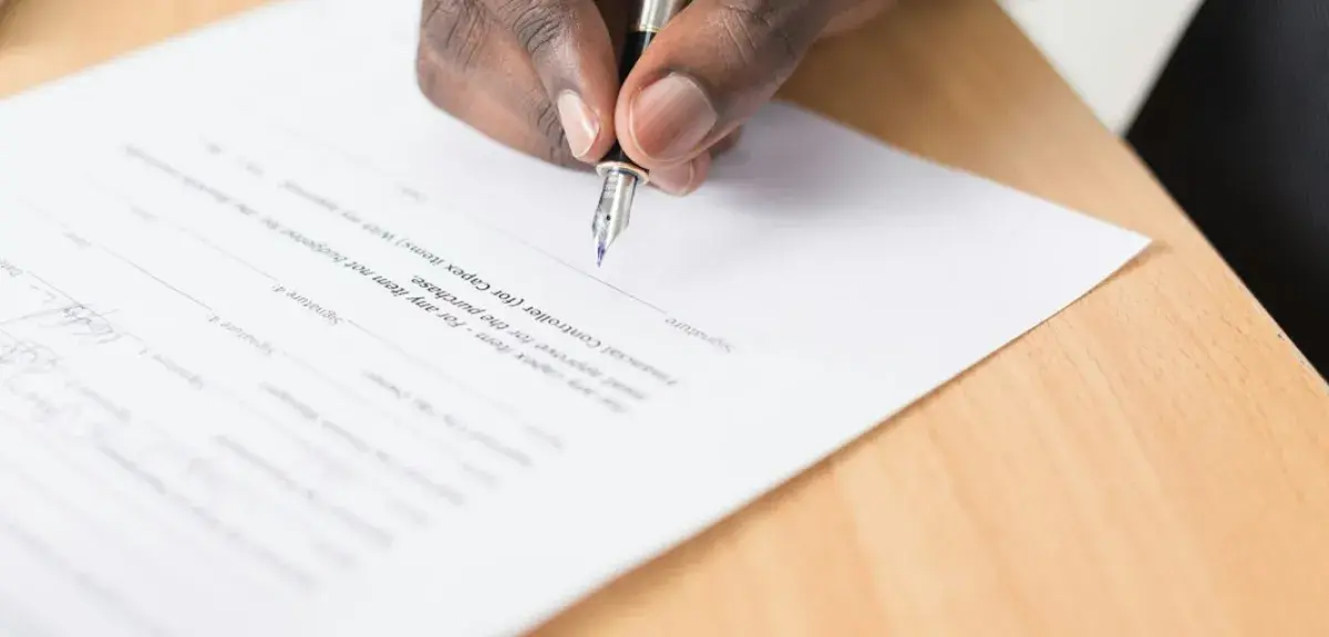 Personne remplissant un document à la main sur un bureau