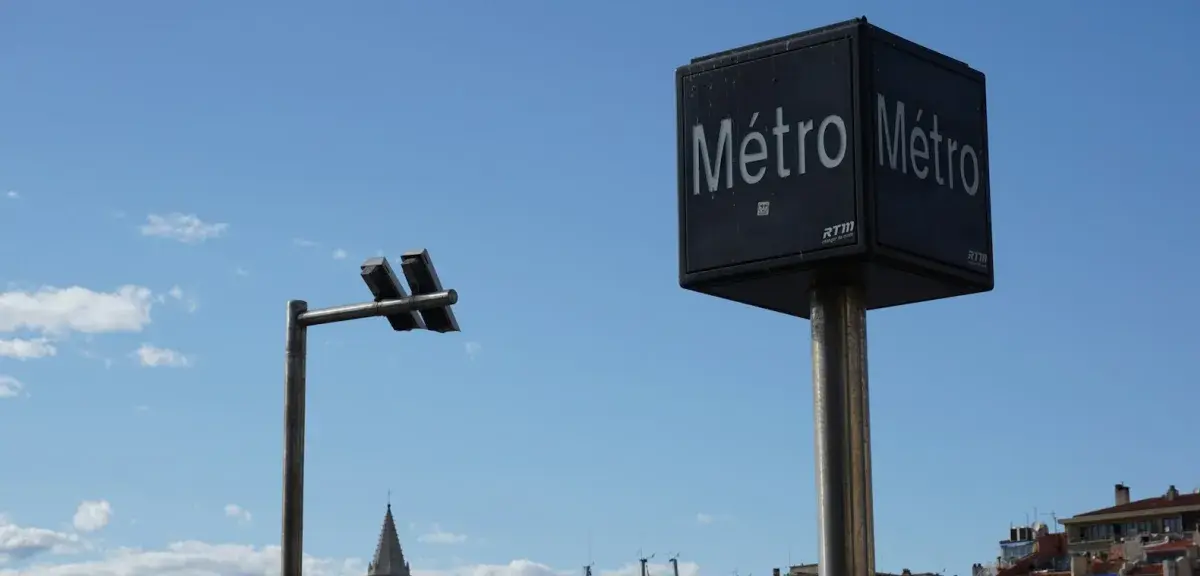 Panneau « Métro » de la RTM sous un ciel bleu à Marseille, avec les toits de la ville en arrière-plan