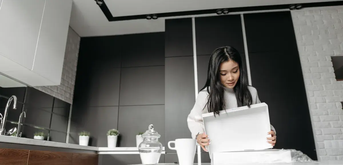 Une femme déballe un colis dans une cuisine moderne après une commande en ligne