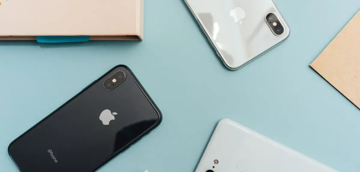 Deux iPhone vus de dos et un autre smartphone posés sur une table bleue