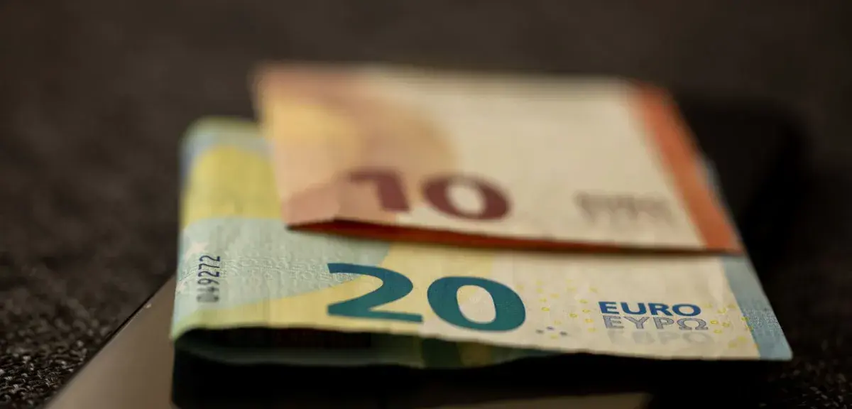 Billets de dix et vingt euros posés sur un smartphone à écran éteint