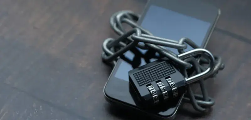 Close-up of a smartphone wrapped in a chain with a padlock, symbolizing strong security.