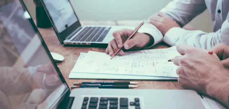 person holding pencil near laptop computer