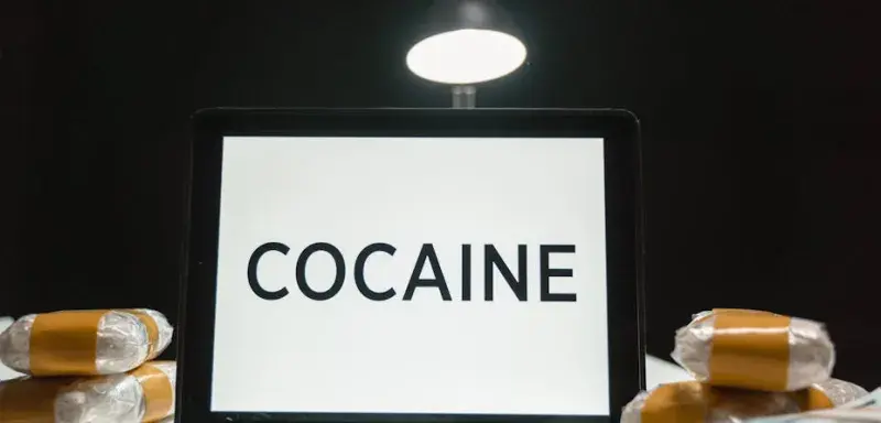 Tablette affichant le mot Cocaine entourée de paquets emballés dans un décor sombre