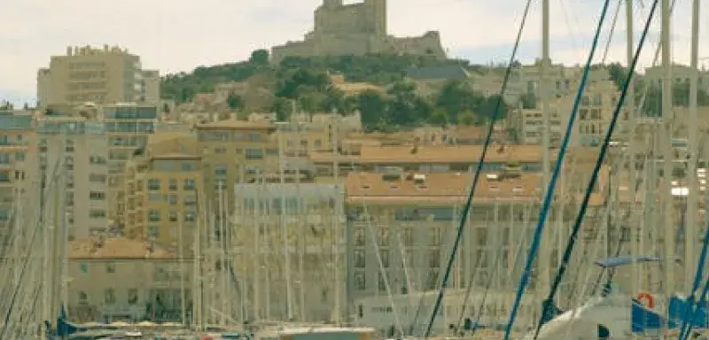 Capture of Marseille's Old Port with yachts and distant view of Notre-Dame de la Garde on a sunny day.