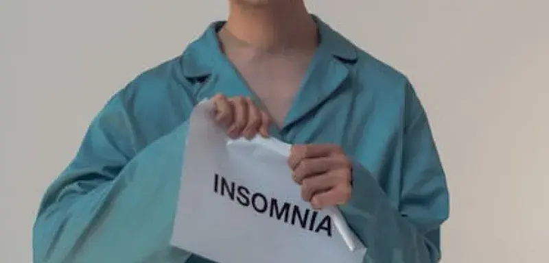 Jeune homme en pyjama tenant une pancarte Insomnia, illustrant les troubles du sommeil