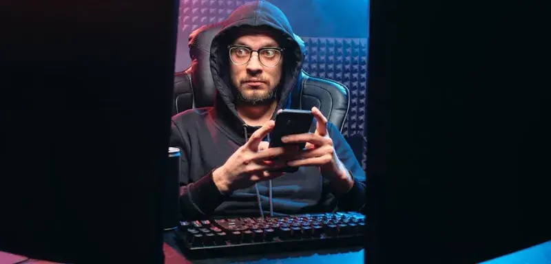 Un homme utilisant un smartphone entouré d'équipements technologiques dans une pièce sombre