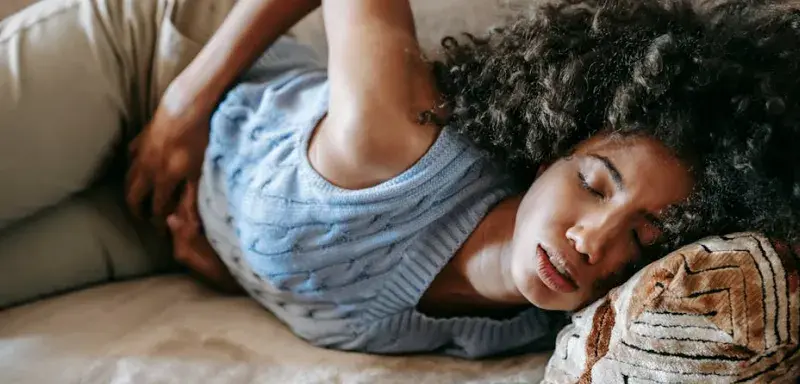 Femme afro-américaine allongée sur un canapé, les yeux fermés, souffrant de douleurs menstruelles