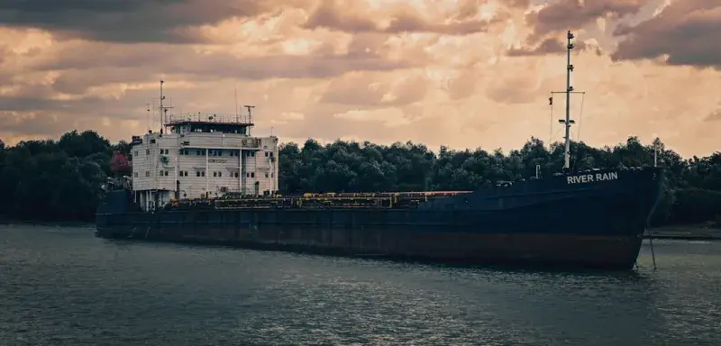 Navire cargo naviguant sur une rivière sous un ciel nuageux