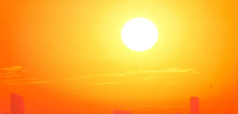 A city skyline silhouetted against a vivid, orange sunset sky.