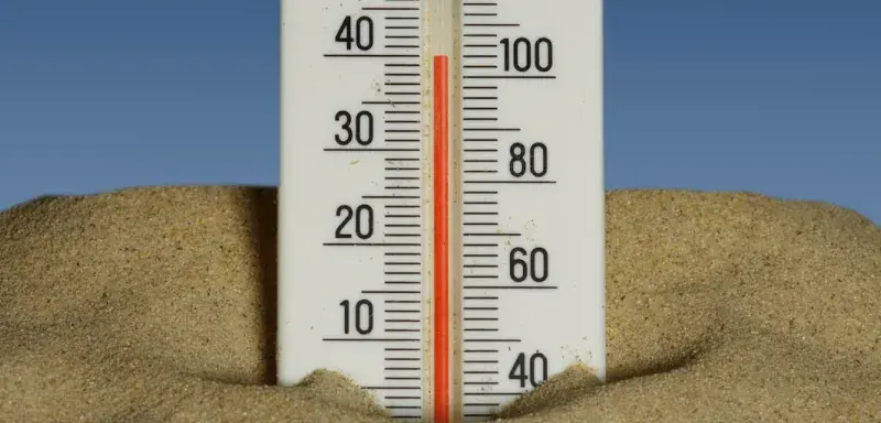 A thermometer in the sand with a blue sky in the background