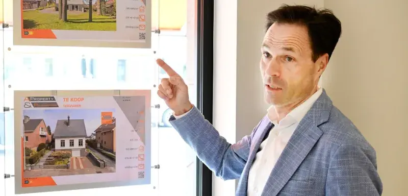 Man pointing at property listings displayed in a window.