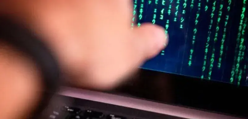 A person points at a glowing code on a computer screen, symbolizing technology interaction.