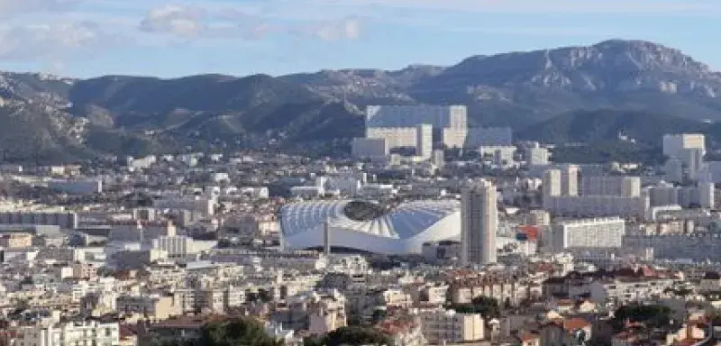 Scenic aerial view of Marseille, France, showcasing urban architecture and distant mountain ranges under a clear blue sky.