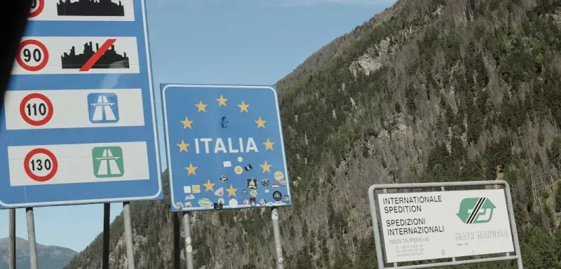 Road signs for italy and eu at a mountain border.