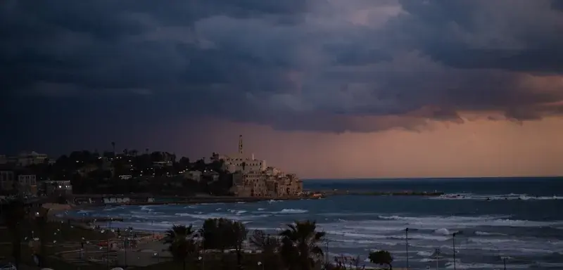 a storm rolls in over the ocean with a city in the distance
