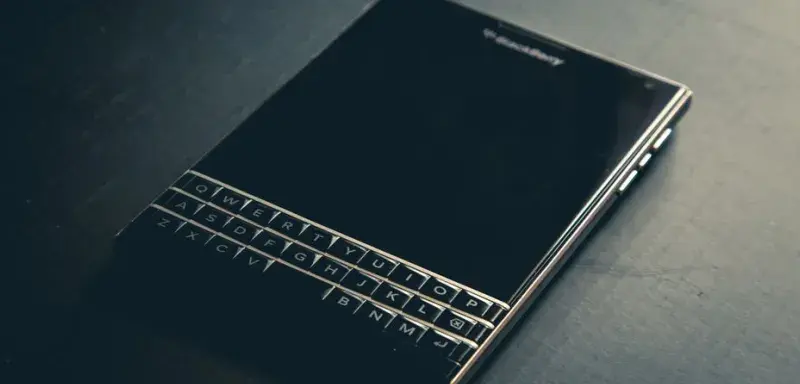 Close-up of a BlackBerry Passport smartphone with a physical keyboard on a dark surface.