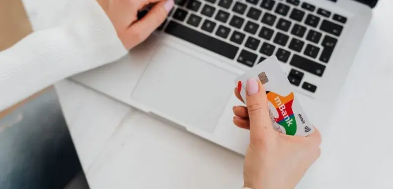 Close-up of a person using a laptop and holding a credit card for online shopping.