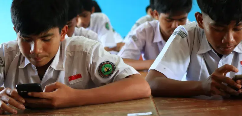 Students in uniform using smartphones in classroom