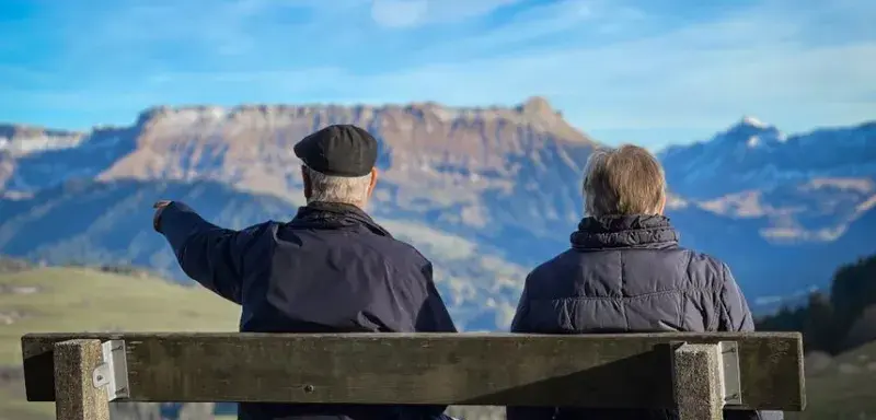 Senior couple sits on bench admiring Swiss Alps landscape in Lucerne.