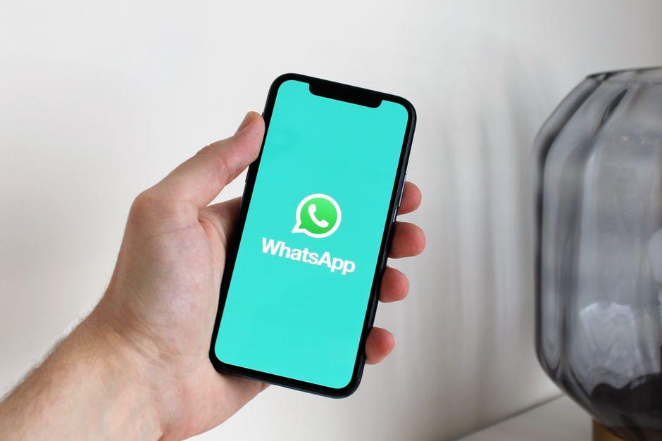 Main tenant un smartphone affichant l'application WhatsApp