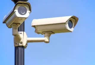 Caméras de surveillance extérieures montées sur un poteau sous un ciel bleu, assurant une surveillance vigilante
