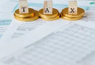 Pièces de monnaie dorées posées sur des documents fiscaux avec des lettres formant le mot taxe