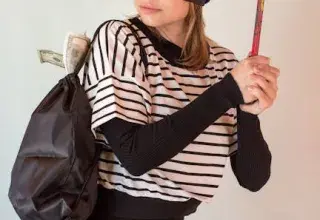 Une femme portant un masque de voleur et un bonnet, tenant un pied-de-biche et un sac avec de l'argent qui dépasse