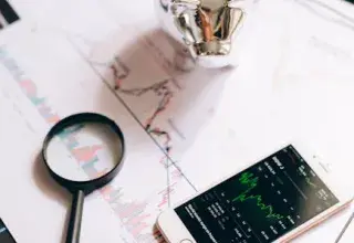 Un smartphone affichant des graphiques boursiers, une tirelire et une loupe sur des documents financiers