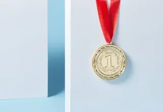 Close-up of a gold medal with a red ribbon hanging against a light blue background.