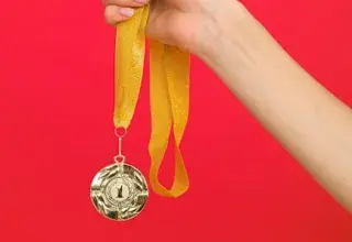 Une main tenant une médaille d'or avec un ruban jaune sur fond rouge vif, symbole de victoire olympique