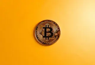 Gros plan sur une pièce de Bitcoin posée sur un fond jaune vif, symbolisant la monnaie numérique
