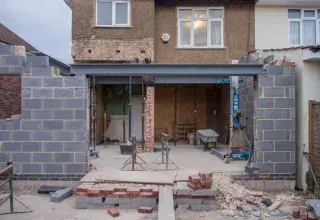 Maison en briques en cours de rénovation avec une extension visible et des matériaux de construction sur le chantier