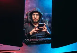 Un homme utilisant un smartphone entouré d'équipements technologiques dans une pièce sombre