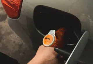 Close-up of a hand refilling a car at a gas station during daylight.