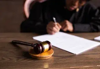 Juge signant des documents au bureau, marteau au premier plan, illustrant la justice.