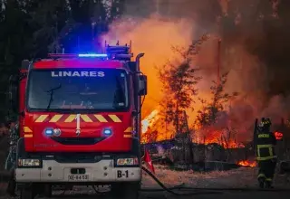 Intense forest fire scene with firefighters and bright red firetruck in action.