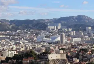 Scenic aerial view of Marseille, France, showcasing urban architecture and distant mountain ranges under a clear blue sky.