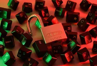 An open padlock surrounded by scattered black computer keyboard keys under red and green light