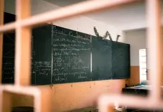 A classroom with a blackboard displaying mathematical equations in French, seen through a window.