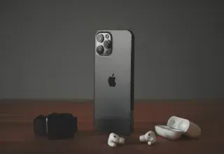 A smartphone, a smartwatch, and wireless earbuds on a wooden surface